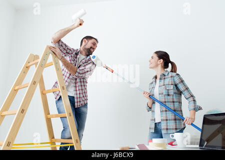 Giocoso coppia felice pittura la loro nuova casa e divertirsi insieme, stanno giocando con i rulli di verniciatura Foto Stock