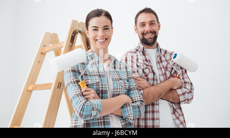 Felice coppia giovane pittura la loro nuova casa, essi sono sorridente e trattenere i rulli di verniciatura Foto Stock