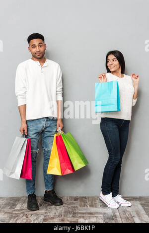 Immagine della giovane coppia amorevole in piedi su parete grigia e tenendo le borse della spesa. Foto Stock