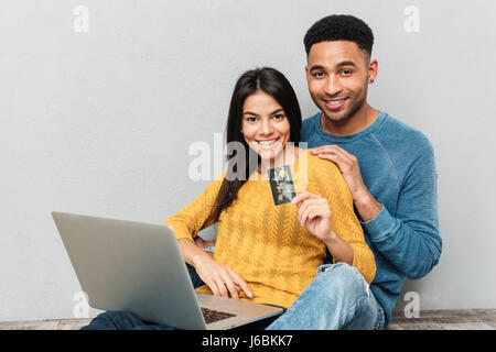 Donna sorridente che mostra carta di credito mentre si utilizza il laptop e seduto vicino al suo uomo isolato Foto Stock