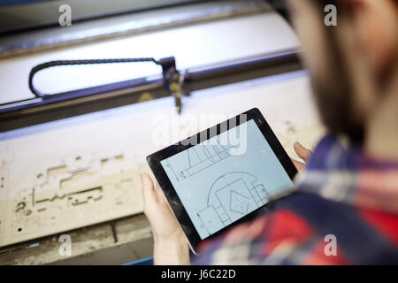 Alta angolazione del lavoratore in fabbrica utilizzando tavoletta digitale per operare il taglio laser macchina in officina Foto Stock