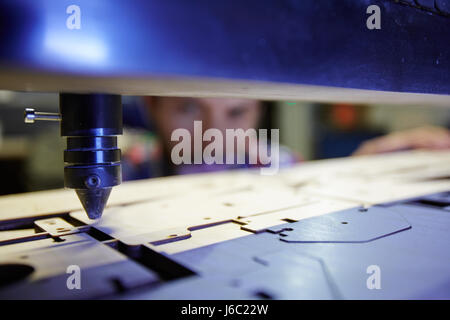 Closeup shot del lavoratore a guardare il fascio laser di taglio di forme complesse da parte di legno in fabbrica Foto Stock