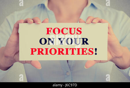 Imprenditrice mani carta bianca segno con focus sulle vostre priorità messaggio di testo isolato sul muro grigio office background. Retrò stile instagram Foto Stock