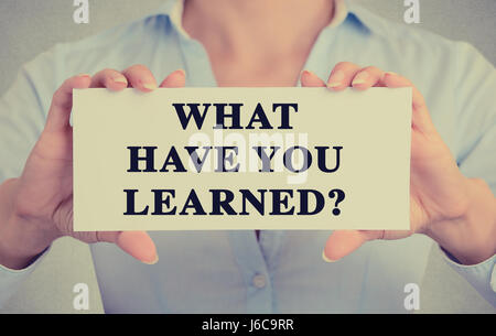 Primo piano maestro mani carta bianca segno con che cosa avete imparato? Il testo della domanda messaggio isolato sul muro grigio office background. Retrò instagr Foto Stock