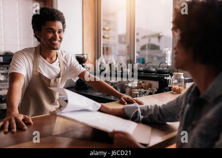 Giovane maschio barista prendendo un ordine da un cliente femmina in un coffee shop e sorridente Foto Stock