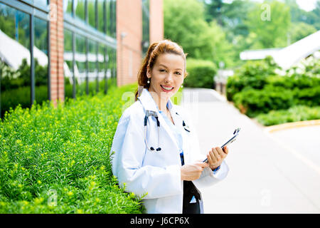 Closeup ritratto giovane femmina fiducioso medico professionista del healthcare holding patient chart sfondo isolato al di fuori del campus dell'ospedale. Visi paziente Foto Stock