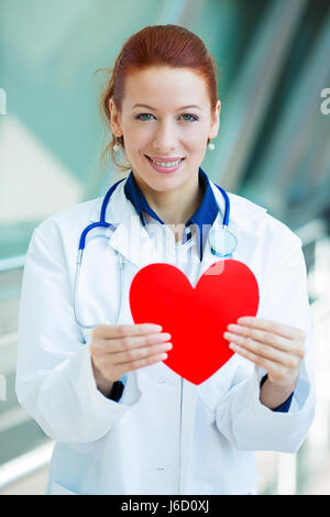 Closeup ritratto sorridenti femmina di professionisti sanitari, donna famiglia medico cardiologo, infermiere con uno stetoscopio holding cuore rosso, isolato h Foto Stock