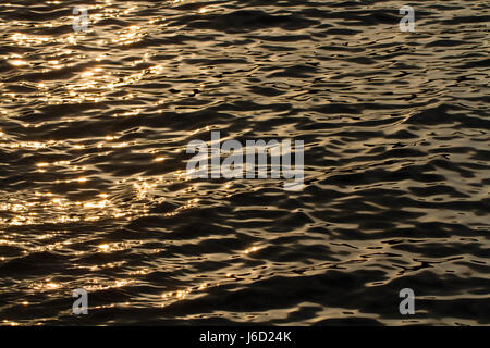 Telaio completo della superficie di un oceano tranquillo di notte con sfarfallio luce solare arancione luccicante sulla superficie in una natura immagine di sfondo. Foto Stock
