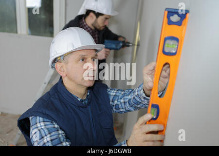 Operaio edile controlla il livello sulla parete Foto Stock