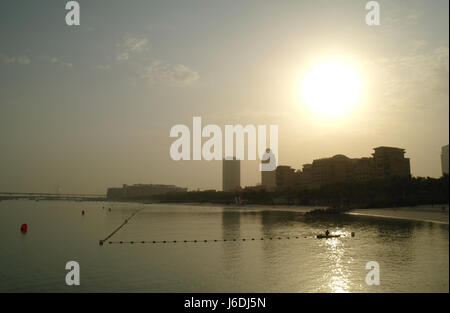 Uomo in canoa Regolazione divisore di nuoto net, verso il sorgere del sole su hotel Westin, Mina Seyahi Beach Resort, dubai, Emirati arabi uniti Foto Stock