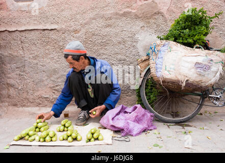 Marrakech, Marocco - 04 maggio 2017: marocchina uomo sta disponendo le sue verdure su un tappetino sulla strada con il suo marocchino tè alla menta al suo fianco. la sua bicicletta Foto Stock