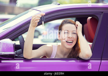 Closeup ritratto felice, sorridente, giovane donna attraente, acquirente seduto nel suo nuovo auto viola che mostra i tasti isolato al di fuori del concessionario, concessionaria molto offi Foto Stock