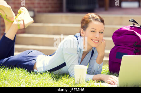 College studentessa sdraiati su un prato erba lavorando sul computer portatile presso il campus universitario al di fuori su soleggiate giornate estive. Istruzione, concetto tecnologico. Il pos Foto Stock