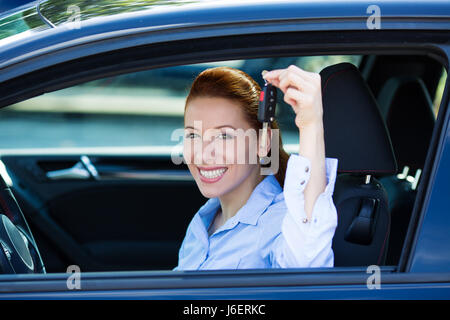 Closeup ritratto felice, sorridente e giovane donna attraente, acquirente seduto nel suo nuovo auto nera che mostra i tasti isolati city street concessionaria backgrou lotto Foto Stock