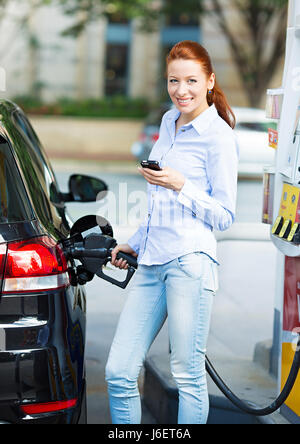 Ritratto sorridenti piuttosto, donna attraente compatto di riempimento serbatoio auto a benzina a gas station isolato sullo sfondo della città. I prezzi del petrolio economia, ener Foto Stock
