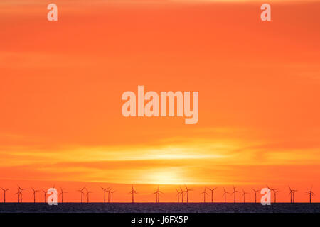 Orange alba cielo sopra il Thanet per centrali eoliche offshore con fila di turbine onon all'orizzonte. Le turbine eoliche stagliano contro il luminoso cielo arancione. Foto Stock