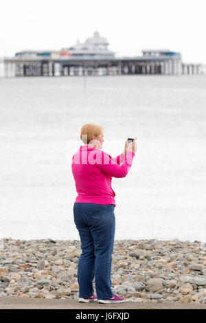 Una donna la definizione di una foto con il suo telefono cellulare fotocamera attraverso la baia di Llandudno Pier in background nella località costiera comune di Llandudno nel Galles del Nord Foto Stock