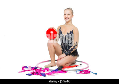 Bella bionda teen età ragazza ginnasta con palla, nastro, hula hoop e machete seduto sul pavimento. Studio shot isolato su sfondo bianco. Copia dello spazio. Foto Stock