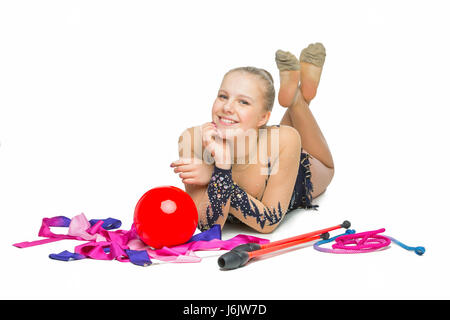 Bella bionda teen età ragazza ginnasta con palla, nastro, hula hoop e machete seduto sul pavimento. Studio shot isolato su sfondo bianco. Copia dello spazio. Foto Stock