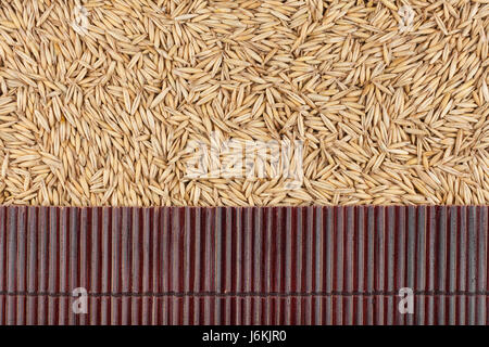 Bello il tappetino di bambù sui cereali di avena come sfondo agricolo. Vista da sopra Foto Stock