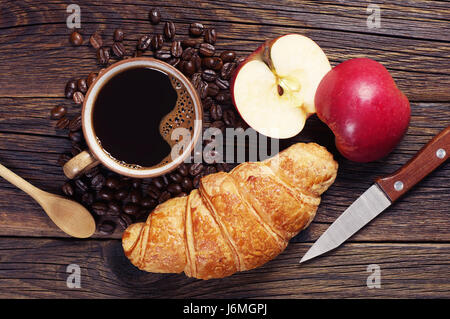 Caffè, croissant e due metà di un Apple al buio su un tavolo di legno, vista dall'alto Foto Stock