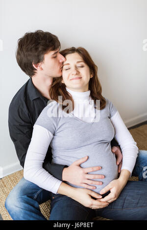 I giovani coniugi in attesa del futuro bambino. L'uomo con tenerezza baci la moglie incinta su di un tempio e abbraccia il suo per un stomaco. Foto Stock