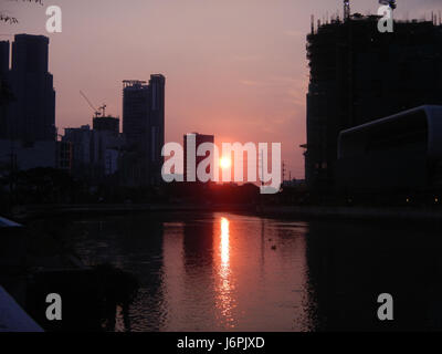 Questa immagine probabilmente cattura il tramonto nelle città di Makati e Mandaluyong, entrambe parte della Metro Manila, conosciuta per i loro vibranti paesaggi urbani e la vivace vita urbana. Il tramonto offre un contrasto visivo con l'ambiente urbano. Foto Stock