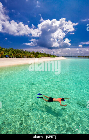 Giovane uomo con la possibilità di fare snorkeling in laguna tropicale con over water bungalow, Maldive Foto Stock