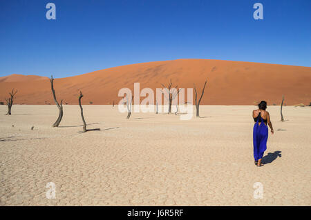 Donna che cammina in un paesaggio desertico con dune e alberi morti, Sossusvlei Salina, Namibia Foto Stock