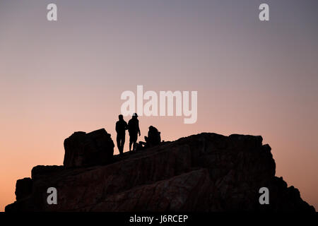 Silhouette di ragazzi distribuivano in cima a una roccia al tramonto. Foto Stock