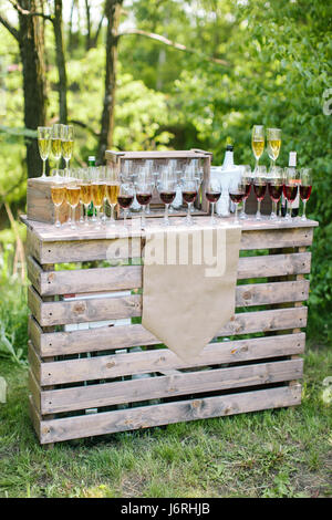 Barra di alcolici in un party in strada nella soleggiata giornata estiva. Bicchieri di vino e champagne su un tavolo di legno contro lo sfondo di verdi. party, matrimoni, compleanni, catering, aperitivo concept Foto Stock