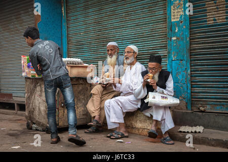 Delhi, India - 10 novembre 2012 - Tre eldery uomini vestiti tradizionalmente parlando con un giovane uomo vestito in abiti alla moda e guardare fuori per lato. Foto Stock