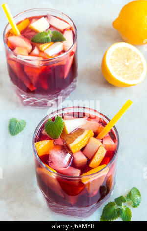 Vino rosso sangria o punzone con frutti, menta e ghiaccio in bicchieri. In casa di frutta rinfrescante sangria oltre rustico tavolo bianco, spazio di copia Foto Stock