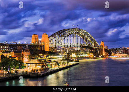 Enorme arcata illuminata del Sydney Harbour Bridge città di collegamento CBD da rocce a nord di Sydney. Luci si riflettono nelle acque sfocata di Sydney H Foto Stock