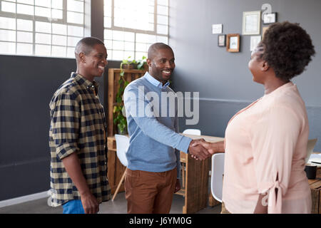 Sorridente africana di colleghi di lavoro che stringono le mani insieme in un ufficio Foto Stock
