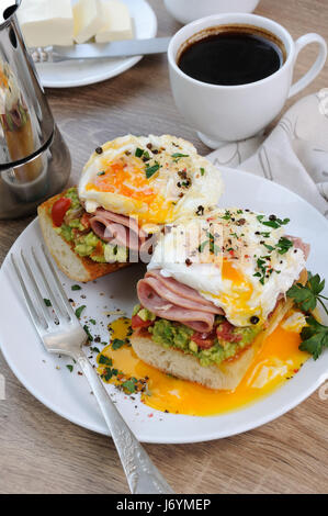 Le uova in camicia con avocado, pomodori, fette di prosciutto su una baguette per colazione