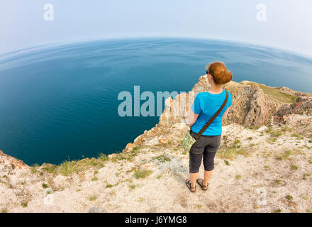 I Capelli rossi ragazza sorge sul bordo di una scogliera sul mare. Foto Stock