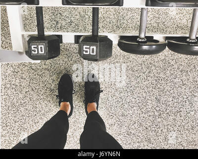 Donna in piedi da rack di manubri in palestra Foto Stock