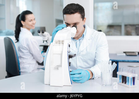 Molto attento assistente di laboratorio che guarda nel microscopio Foto Stock