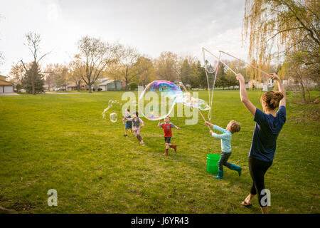 Madre e quattro bambini che giocano con il gigante bolle di sapone Foto Stock