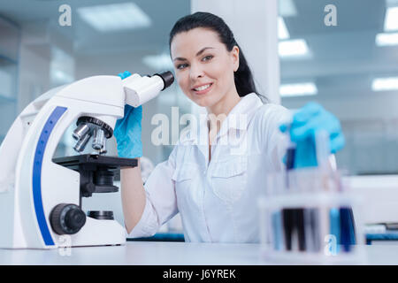 Bella bruna usando microscopio per esaminare i reagenti Foto Stock