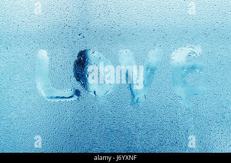 La parola "Amore " con gocce d'acqua sul vetro della finestra. La formazione di condensa sulla finestra. Elevata umidità in camera. Il tono freddo. Foto Stock