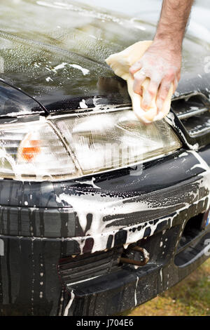 La mano dell'uomo lavaggi delle auto della maschera di spugna di abbondante schiuma. Foto Stock