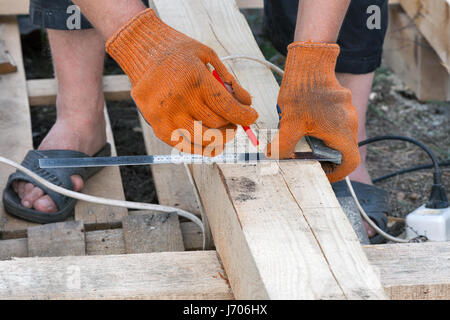 Costruzione cottage di legno. Misurazione di barre di pino con l aiuto di un angolo utensile closeup all'aperto. Foto Stock