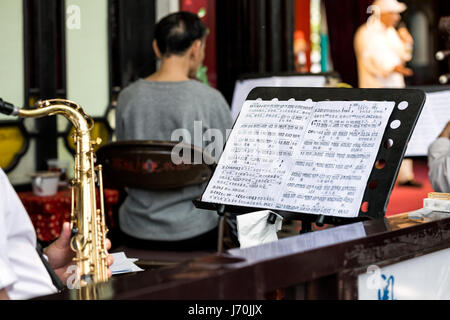 Aprile 2017 - Guangzhou, Cina. Opera Cinese musicista giocando un sassofono tenore durante la lettura di brani di musica cinese foglio. Foto Stock