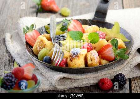 Deliziosa austriaco del 'Kaiserschmarren" (come shredded frittelle dolci) servita con fresca frutta colorata in un ferro da stiro padella sulla biancheria vintage Foto Stock