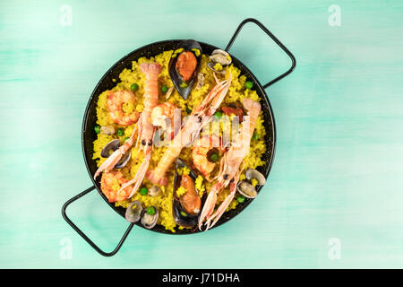 La foto di un pesce spagnolo paella in un tipico paellera, con cozze, vongole e gamberetti, con un posto per il testo, ripresa dall'alto su una texture di teal Foto Stock