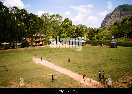 I bambini giocare a cricket presso il locale motivi in Ella, Sri Lanka. La montagna noto come Ella roccia possono essere visti sullo sfondo. Foto Stock