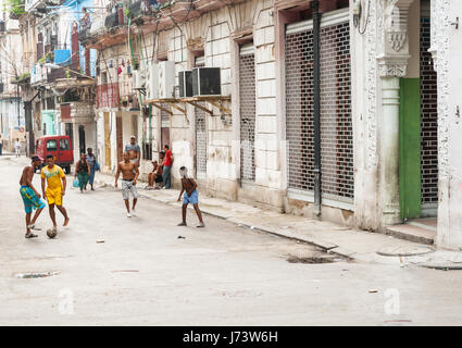 Quattro ragazzi giocare a calcio in strada urbana come persone a piedi da circondata da una schifezza di vecchi edifici abbandonati che mostra segni di povertà negli anni di noi emba Foto Stock