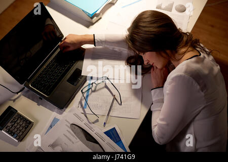 Stanco della donna che dorme sul tavolo per ufficio di notte Foto Stock